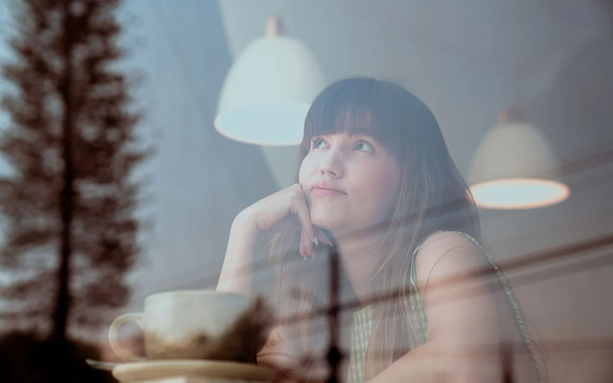 A person looking thoughtfully at their phone by a window, natural light, quiet uncertainty
