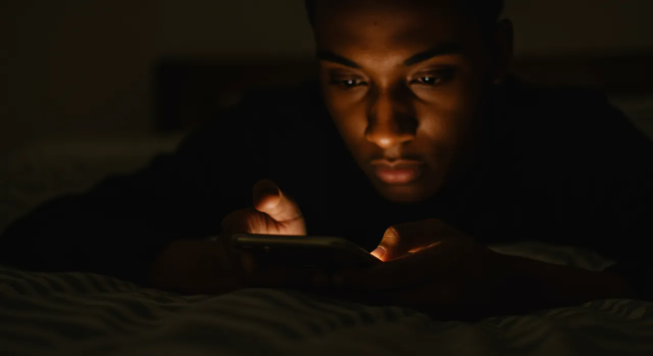 A person's face lit by a smartphone glow while scrolling alone at night