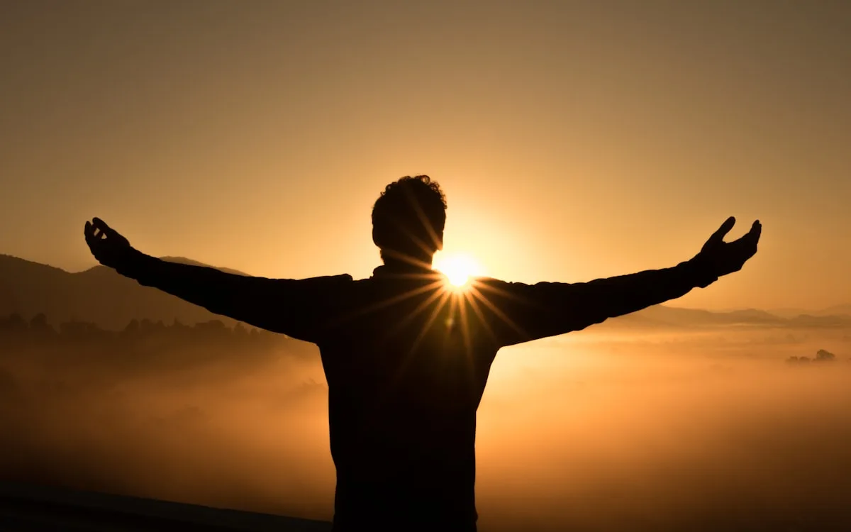 Silhouette of a person standing with arms outstretched at a golden sunrise over misty mountains